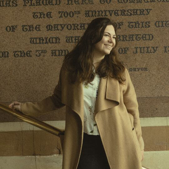 Instagram Photo of Woman with long brown hair smiling while leaning against the exterior wall of Winchester Guildhall.