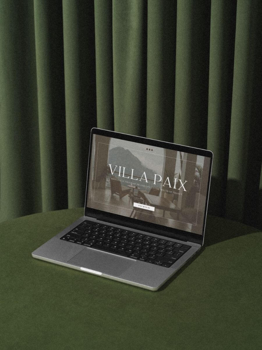 Open laptop on styled against retro green background, displaying website homepage for Villa Paix.